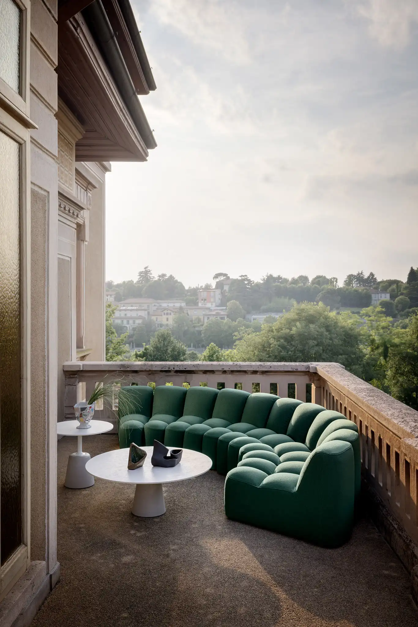 Allestimento di una terrazza con divano modulare verde e tavolini in cemento