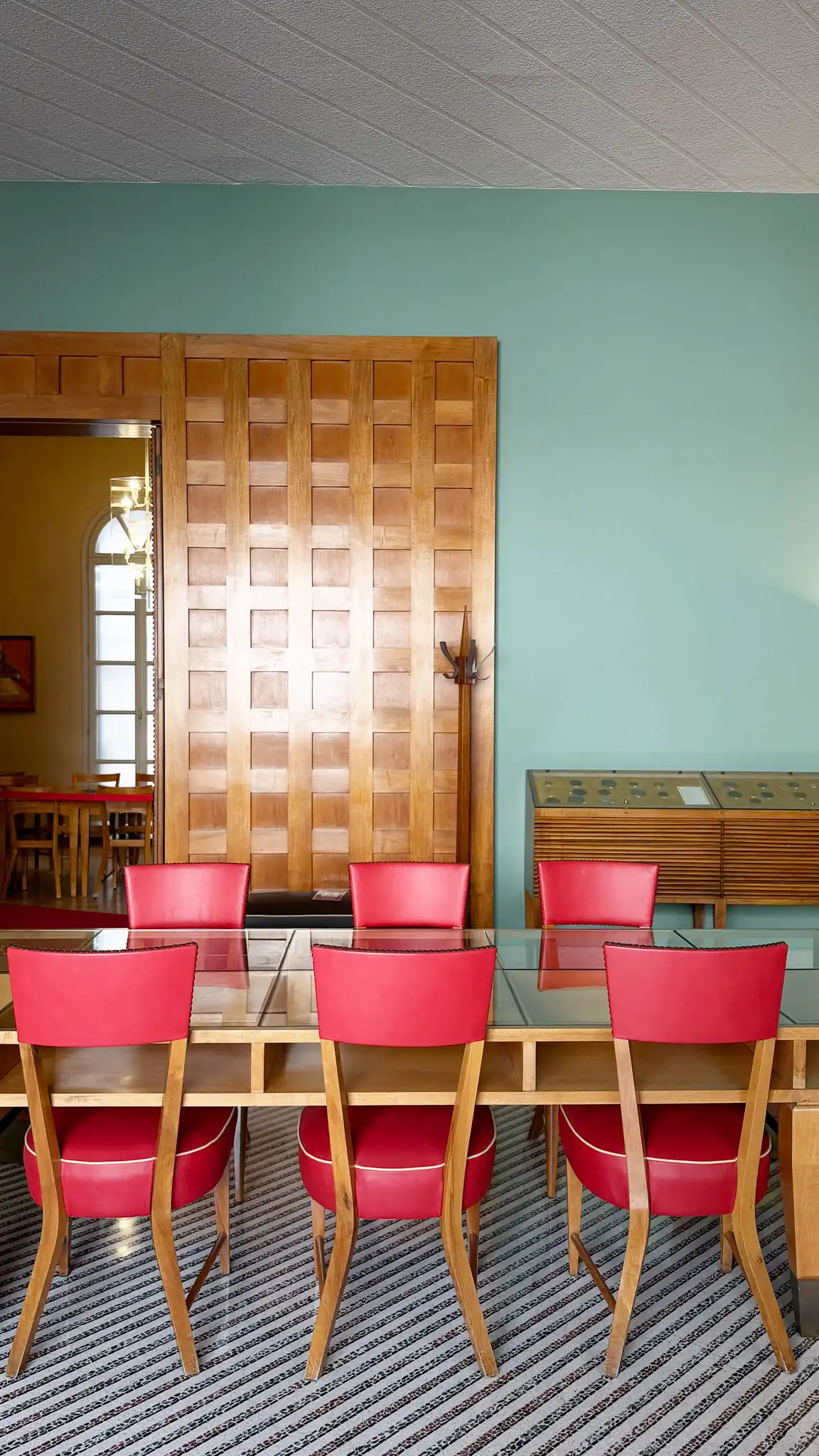 Dettaglio porta cesellata in legno e tavolo con poltroncine in pelle rossa