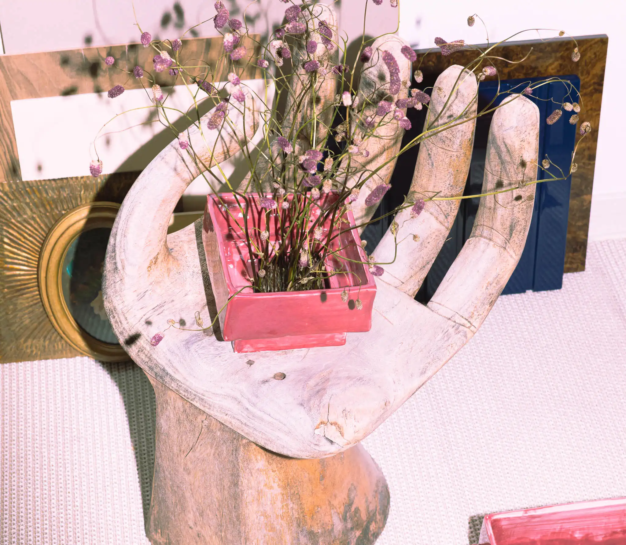 Composizione artistica con seduta a mano in legno e vaso rosa con fiori secchi.