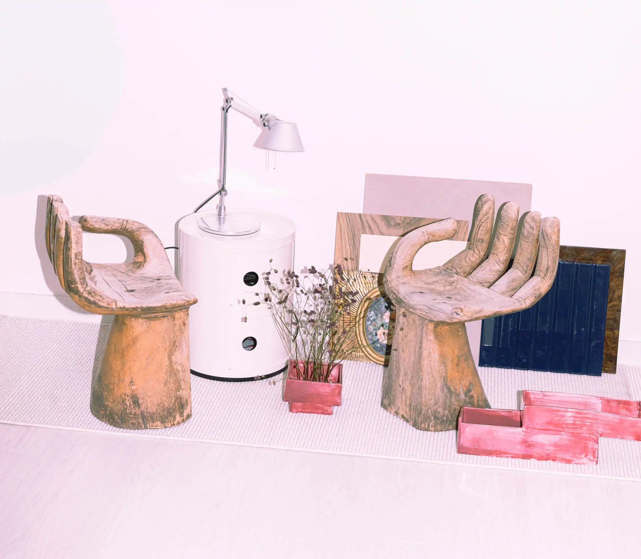 Angolo d'arredo con due sedute artigianali in legno a forma di mano, comodino modernista in plastica con lampada da tavolo metallica e materioteca