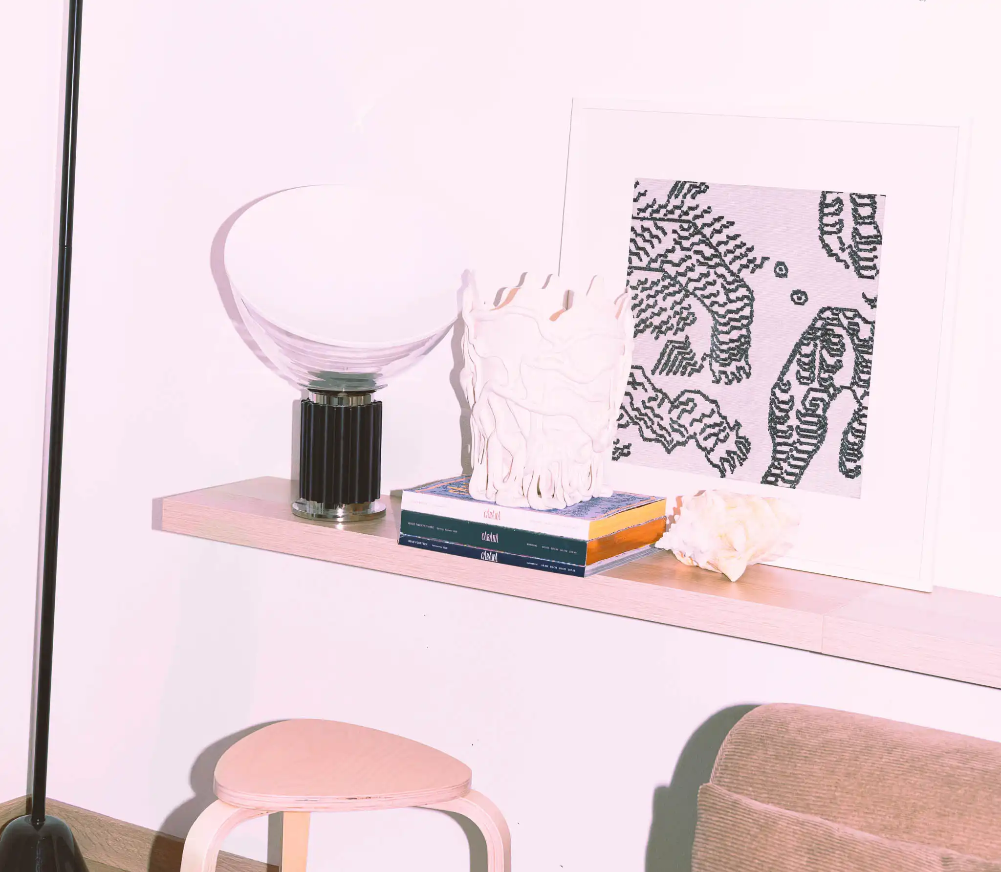 Mensola minimal con lampada Taccia, vaso di design e riviste; arredo chiaro con sgabello scandinavo e dettagli decorativi.