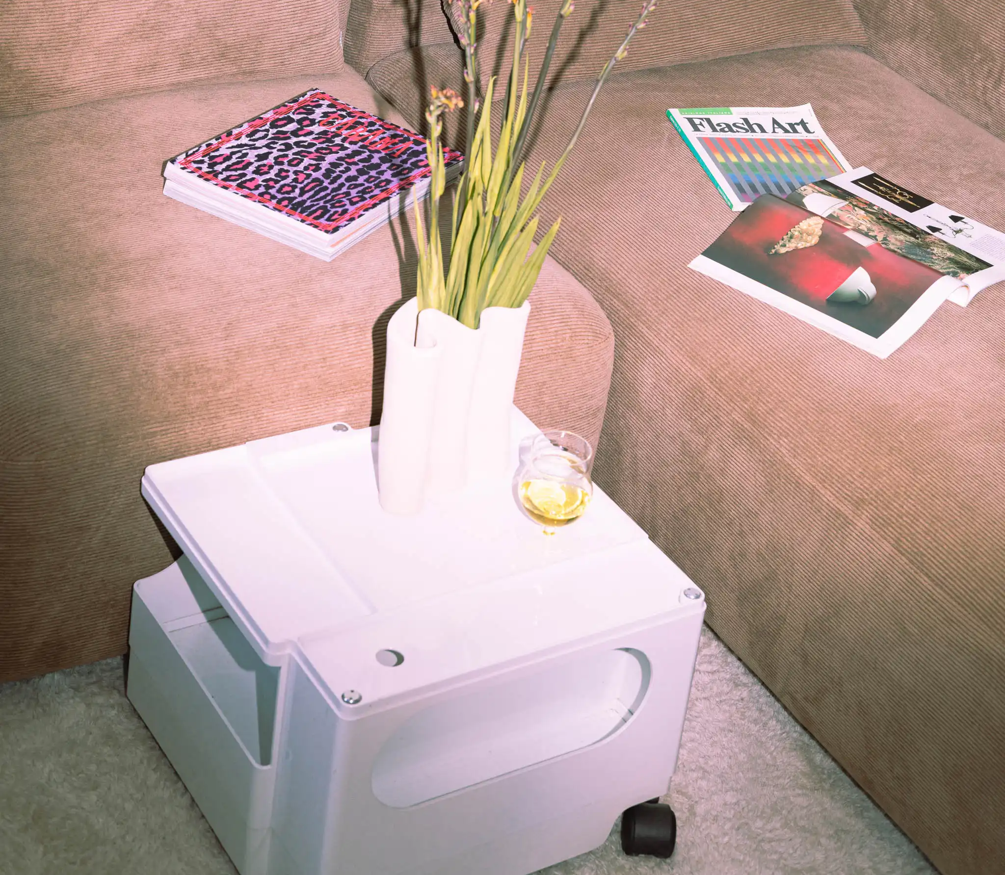 Angolo living con coffee table Bob bianco, vaso con fiori e divano in velluto marrone; sullo sfondo busto blu Klein e tappeto berbero.
